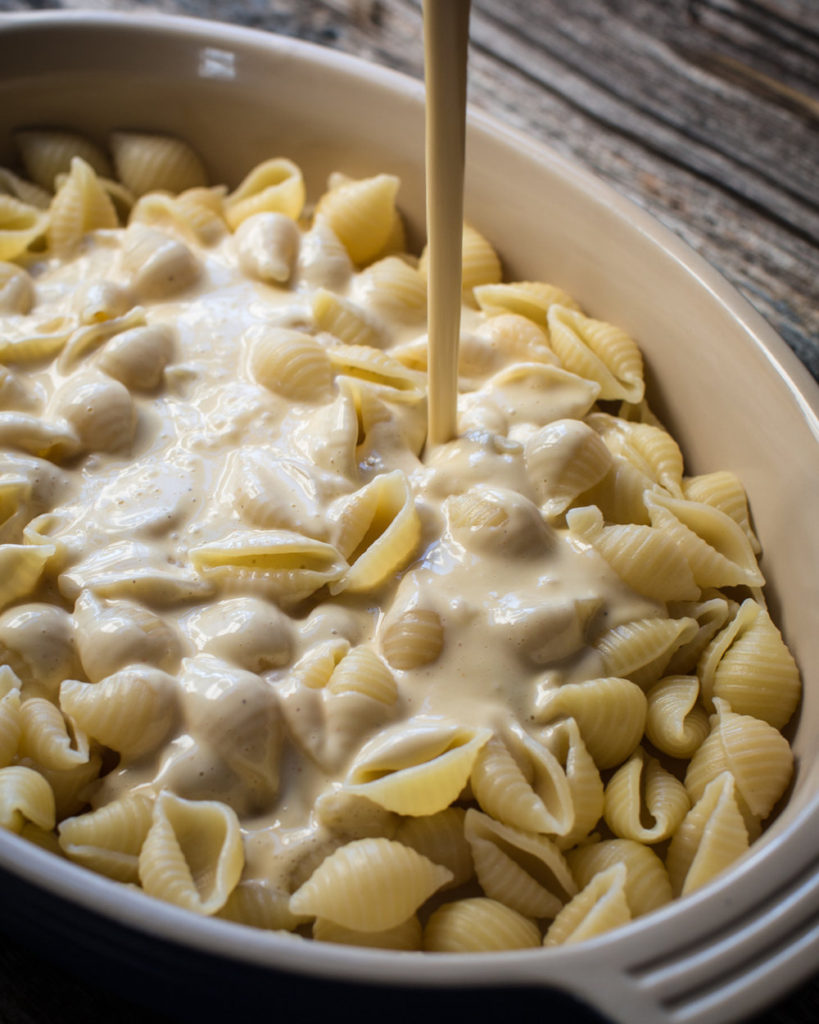 Large pan of white truffle macaroni and cheese with cheese drizzling on shells