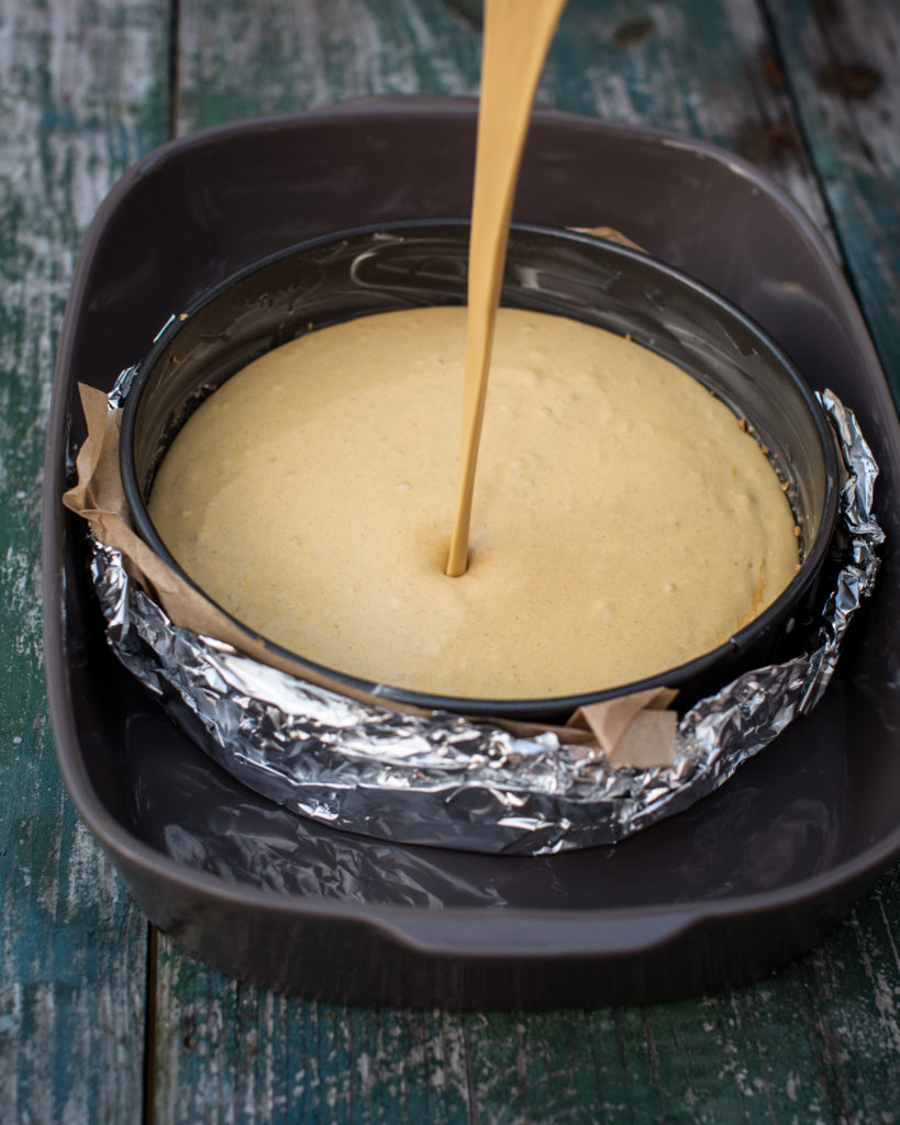 cheesecake batter pouring into a springform pan inside another pan for baking