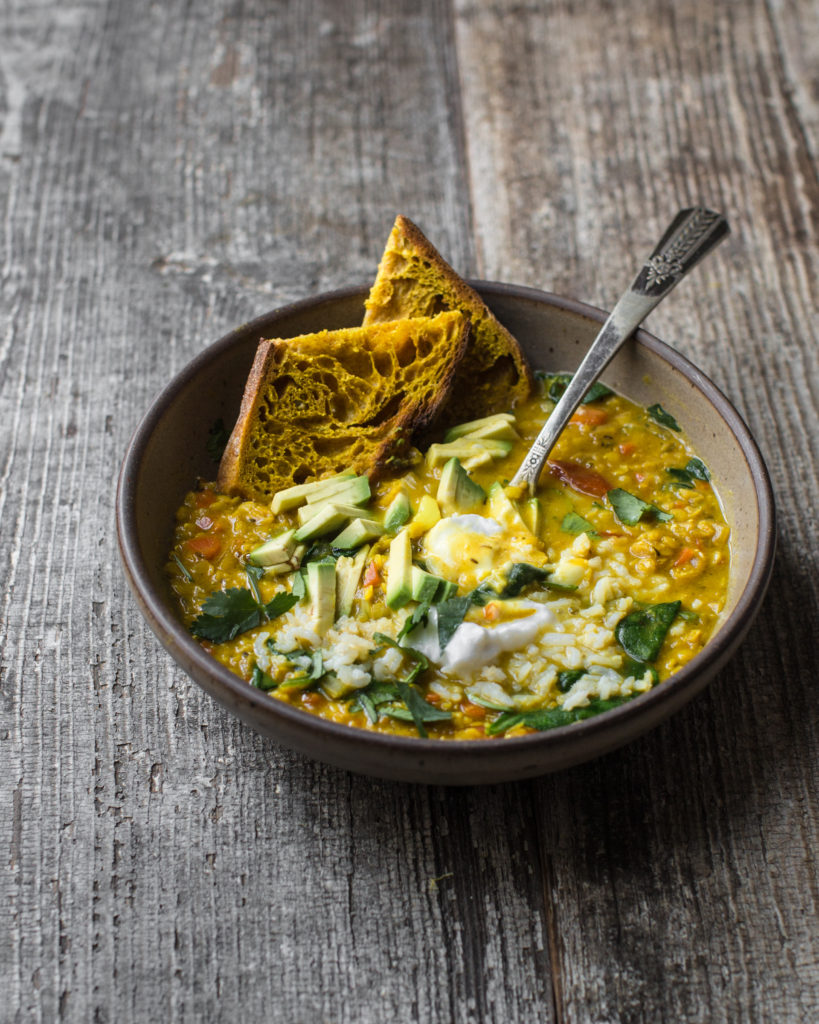 vegan dahl in a bowl with sourdough toast, avocado, and coconut yogurt on a wooden table