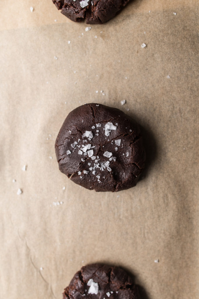 Cookie dough balls with salt on top on parchment paper