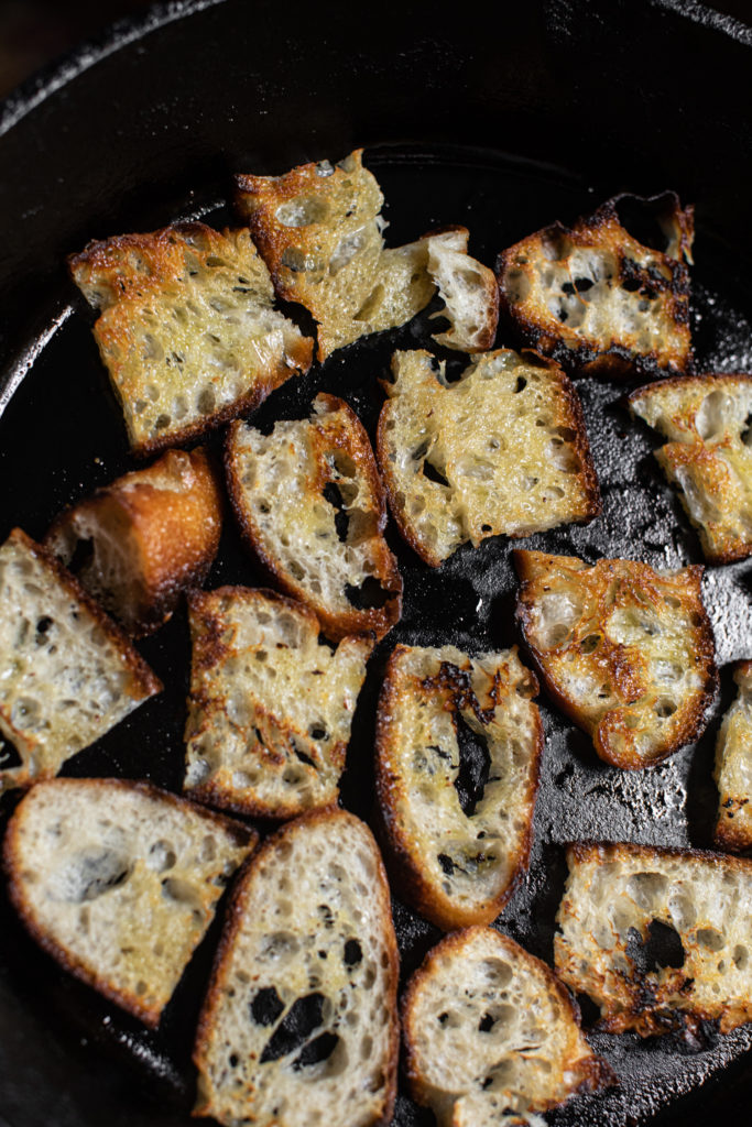 Pieces of bread frying in a cast iron skillet