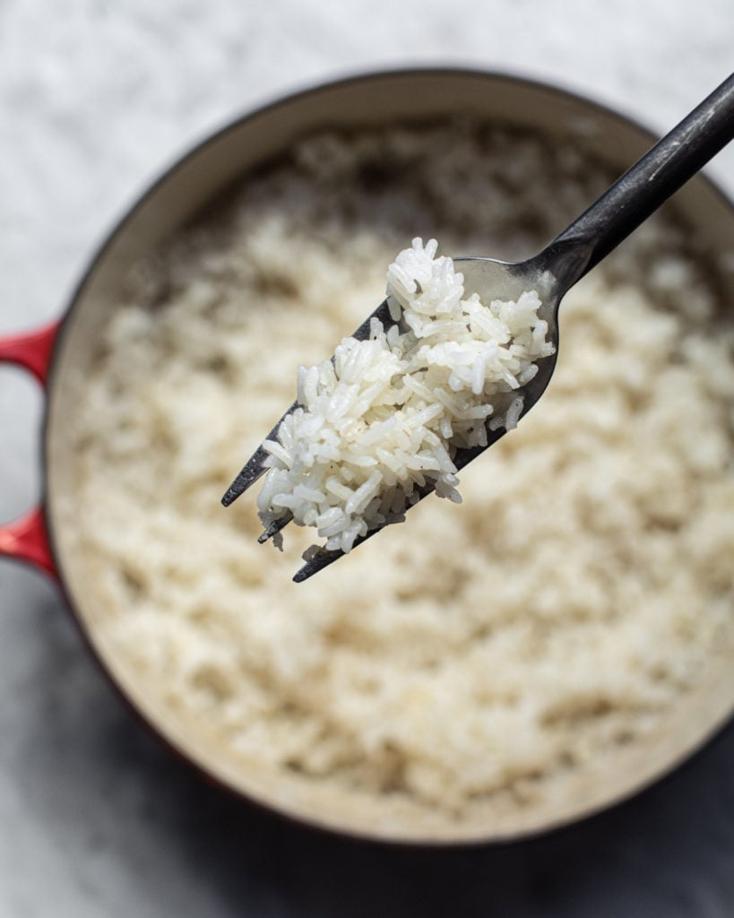 Cooked rice on a fork over a pot of rice