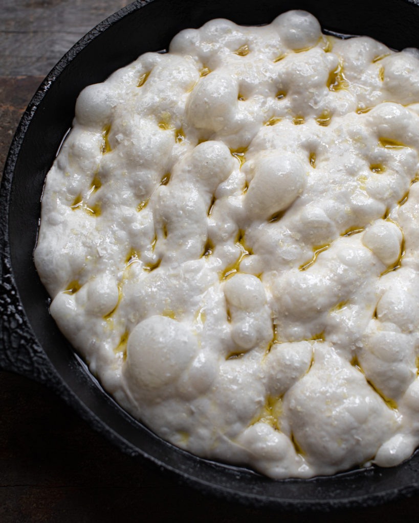 Dimpled sourdough dough in a cast iron skillet with olive oil drizzle