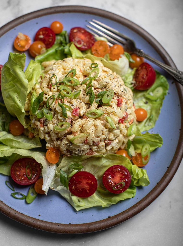 Big scoop of macaroni salad on a bed of greens with tomatoes on a plate