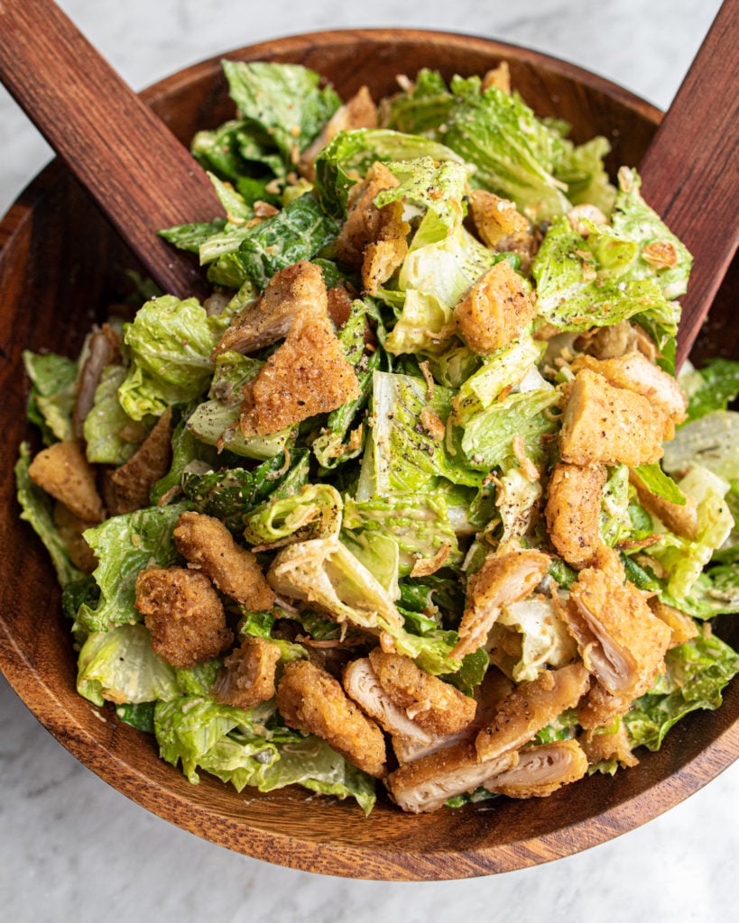 Crispy Chicken Caesar Salad in a wooden bowl with wooden spoons