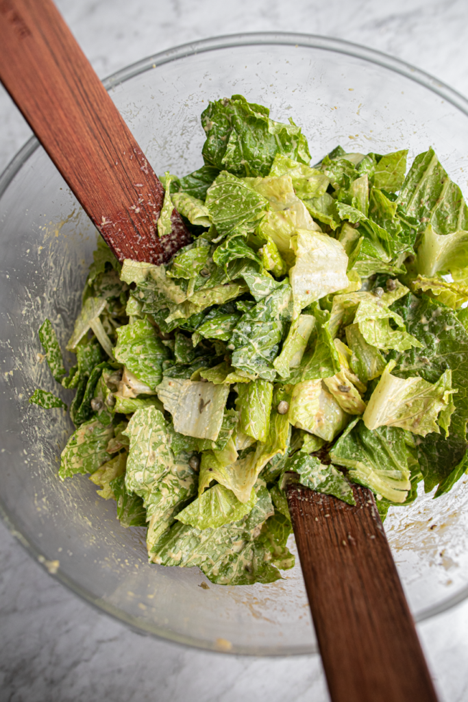 Bowl of romaine lettuce with salad dressing in a mixing bowl with wooden spoons