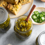 candied jalapenos in a pickling jar with a serving spoon