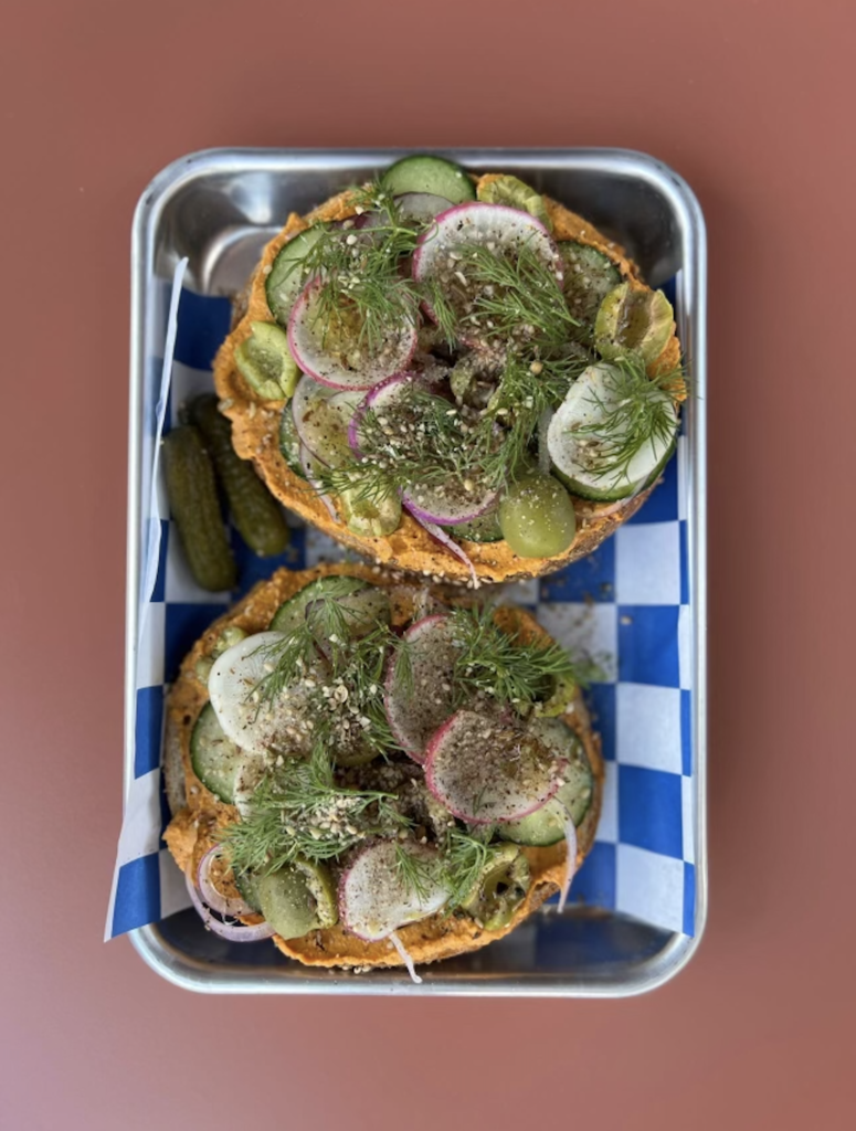 Bagel cut in half with carrot spread and many vegetables