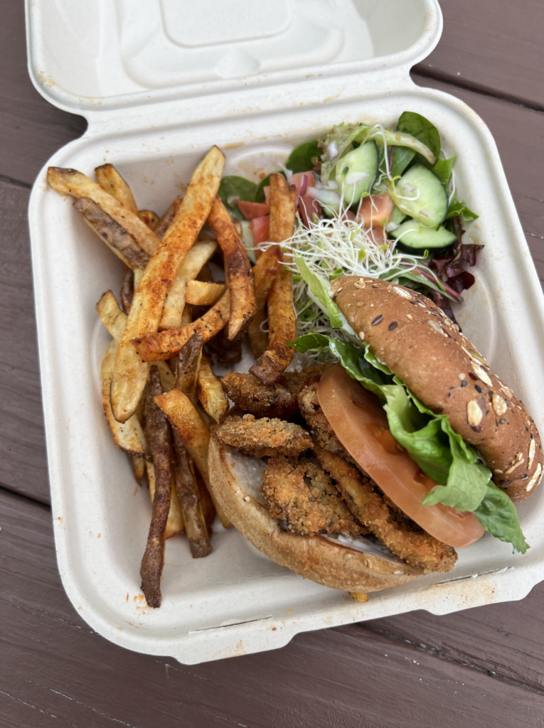 Mushroom sandwich with french fries and a salad in a takeout container