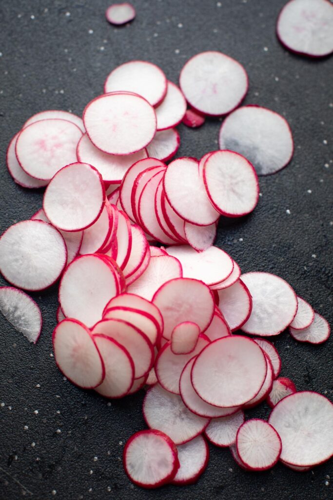 Thinly sliced radishes on a dark cutting board