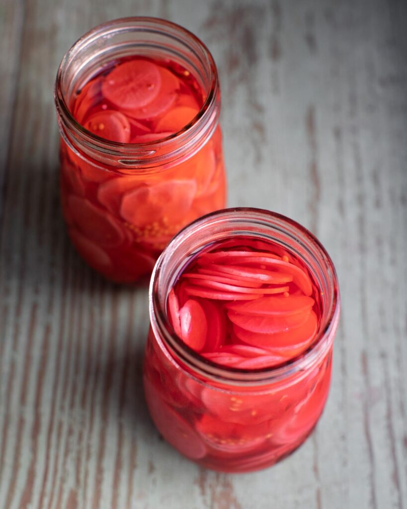 Two open glass jars with sweet pickled radish inside.