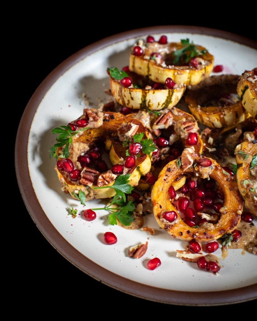Slices of delicata squash topped with pomegranate seeds, and pecans on a white plate
