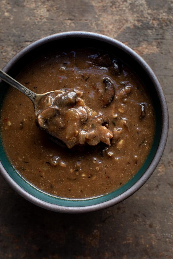 Blue bowl filled with mushroom gravy with a metal spoon sticking out