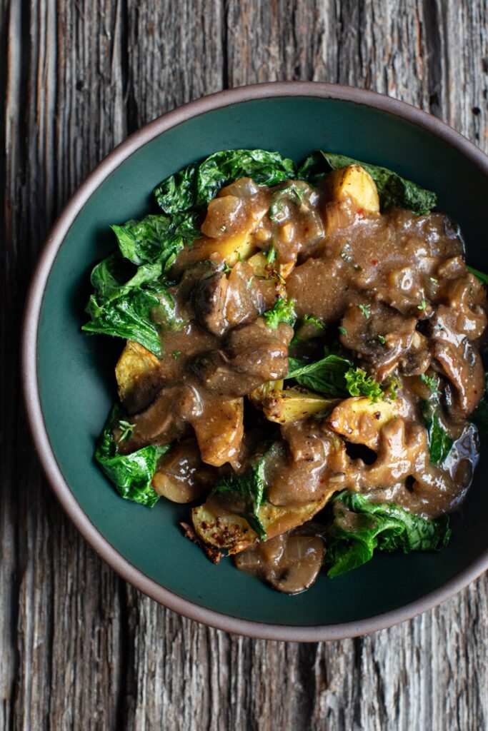 Mushroom gravy drizzled over potatoes and greens on a blue plate