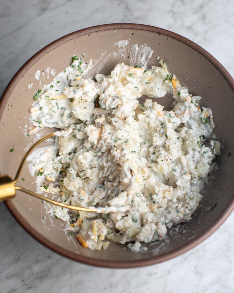 Bowl of shredded cheese, coconut yogurt, and fresh chives mashed together for the filling