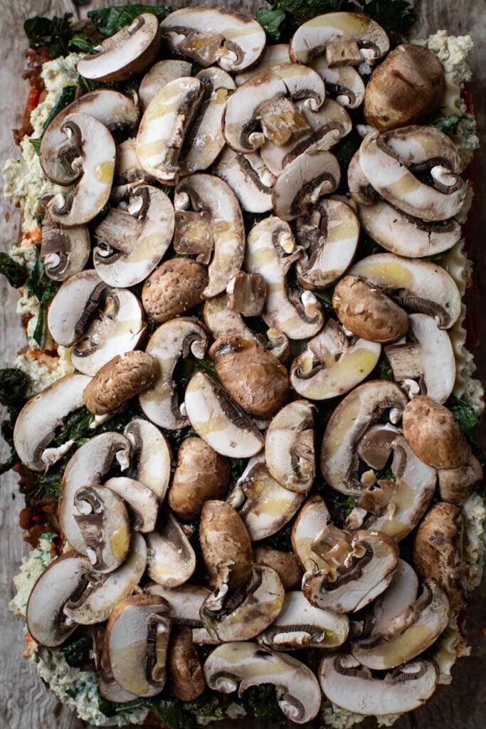 Sliced mushrooms and greens layer in a baking dish.  