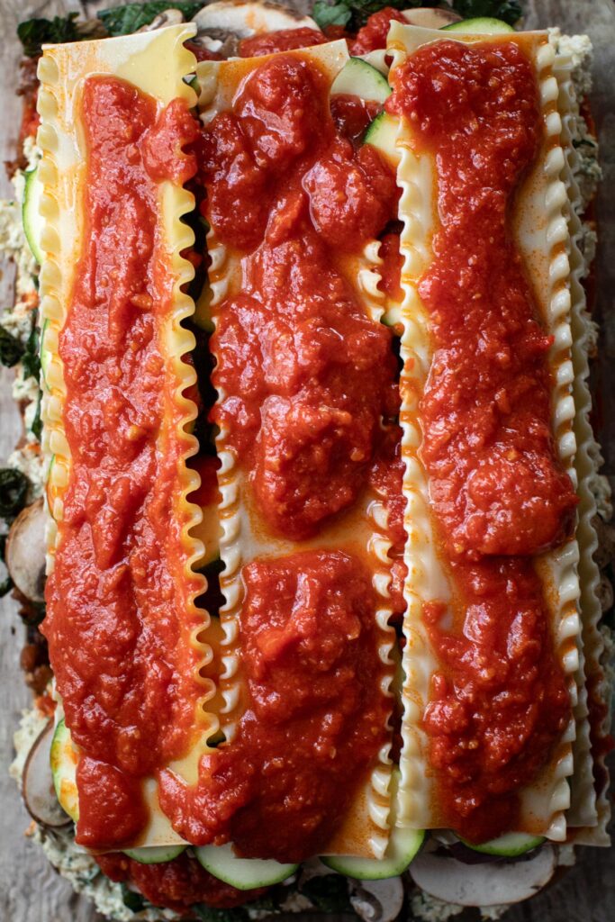 Zucchini, noodles, and marinara layer in a baking dish. 