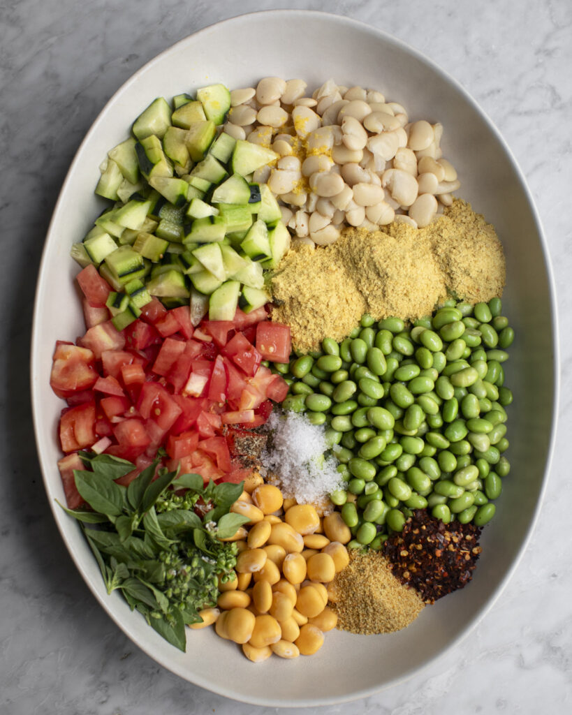 overhead photograph of all of the ingredients for the three bean salad in a large mixing bowl on a marble table
