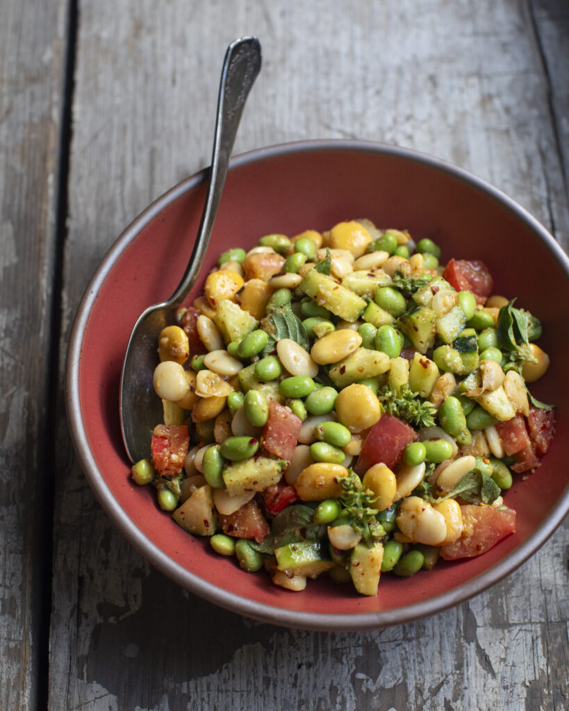 three bean salad in a bowl with a spoon on a wooden table