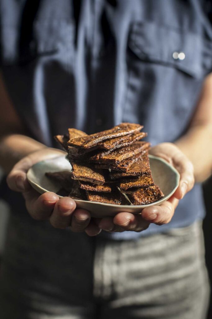 hands holding the finished tofu bacon in a bowl 