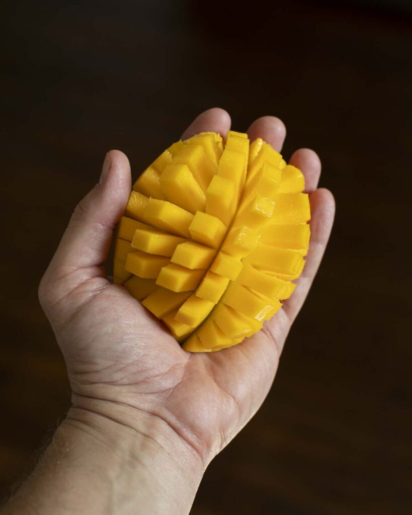 a hand holding a sliced mango