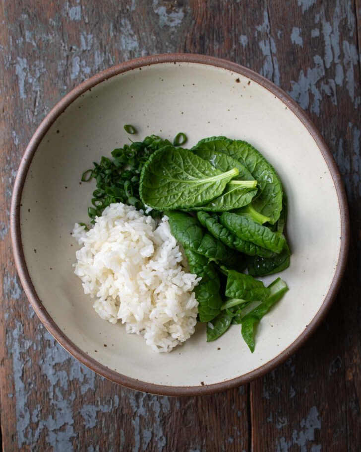 greens, rice, and scallions in a bowl before adding the mung bean soup